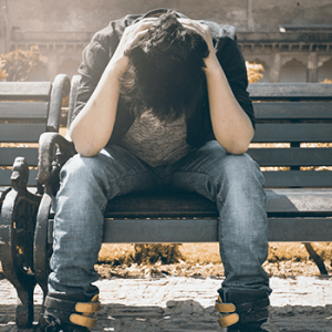 man in black top and jeans holding head down on bench