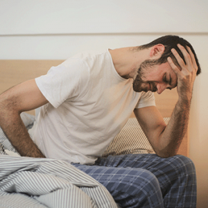 young man sat on bed in sleepwear suffering from headache